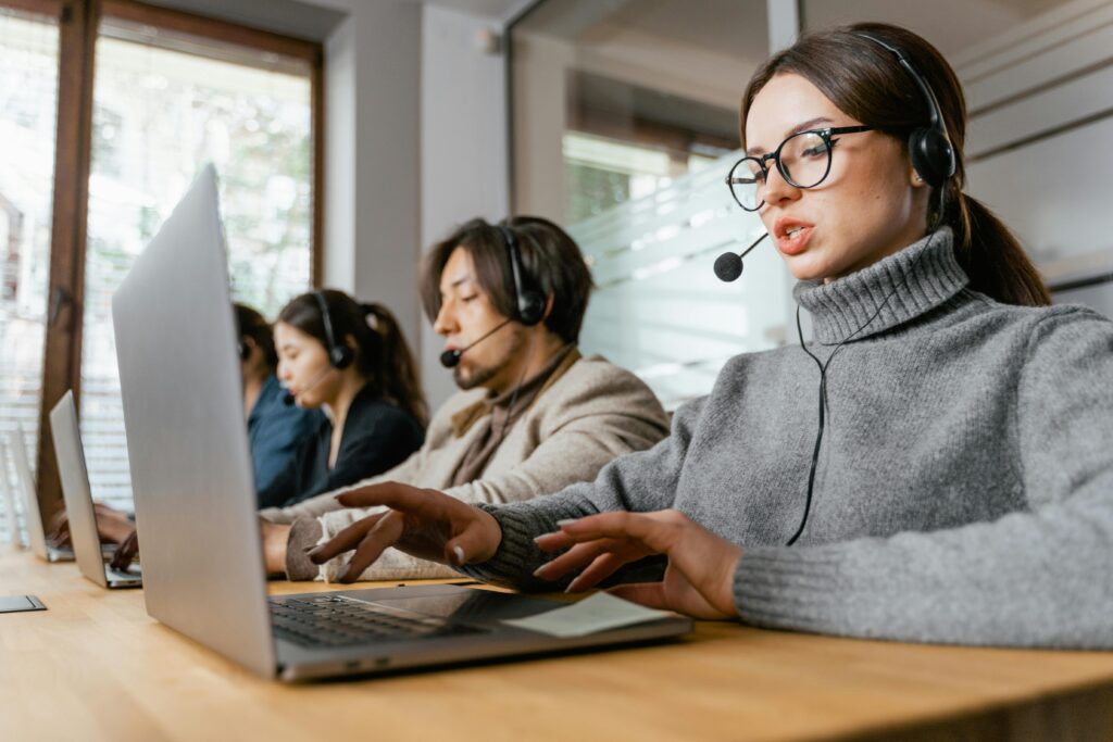 Four call center employees working with headsets and laptops in a modern office setting.