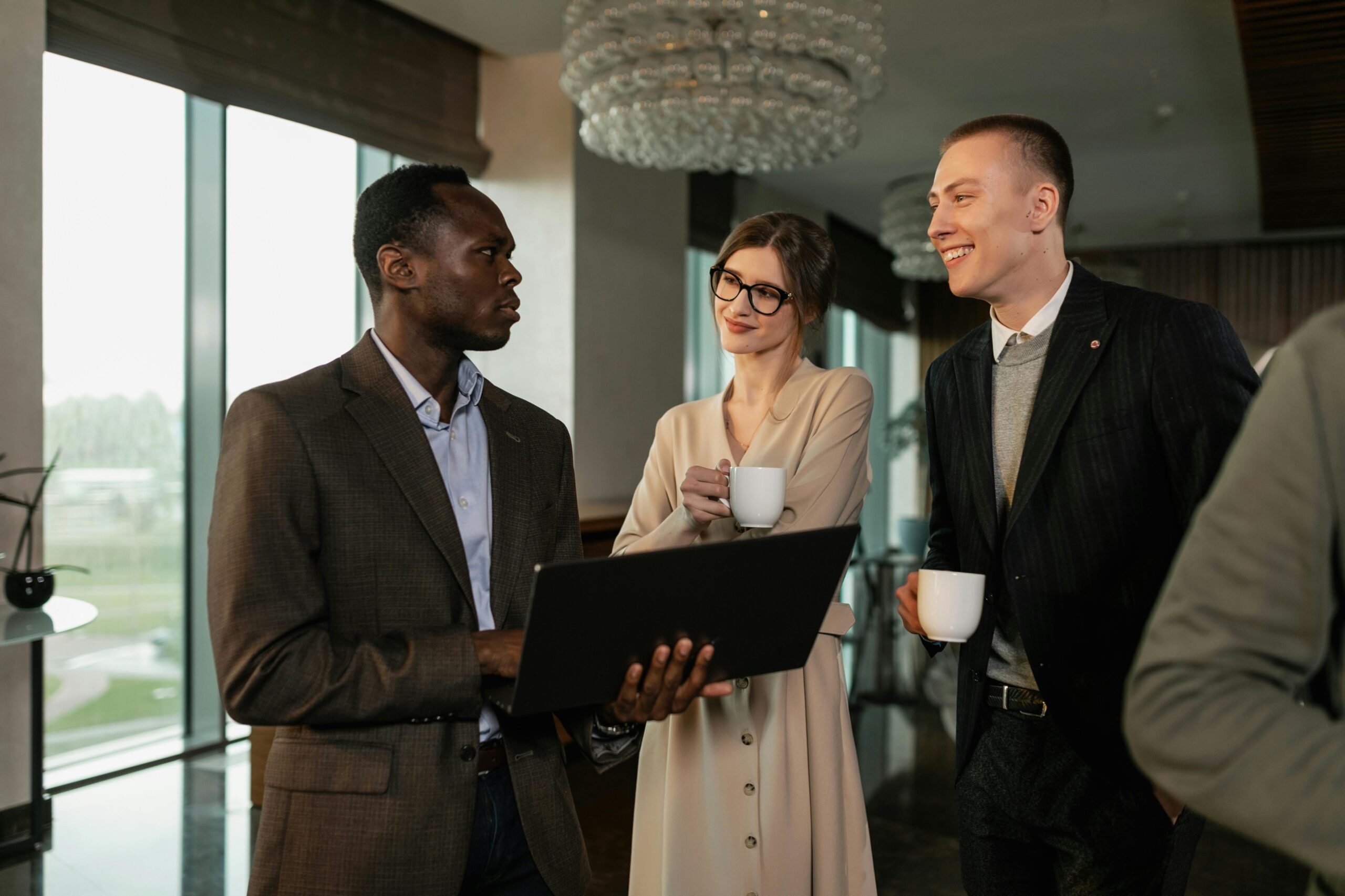 Group of colleagues engaging in a friendly business discussion indoors with laptops and coffee.